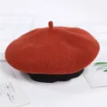Close-up detail shot of the elegant red wool beret featuring a classic black ribbed brim. - Adjustable / Brick Red