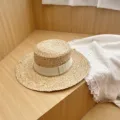 Closeup of a stylish raffia flat top straw hat with beige ribbon on wooden background. - M (56-58cm) / Beige