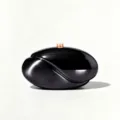 Detailed view of black wave acrylic clutch bag, sleek glossy finish with metal clasp. - Metallic Black