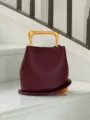 Burgundy leather bucket bag detail featuring a unique rigid gold handle and curved base design. - Burgundy