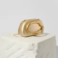 Close-up detail of the gold metallic evening clutch showcasing its unique sculptural handle. - Gold