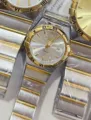 Two-tone quartz watch with Roman numerals bezel, metal strap, and calendar display. - Two-Tone Gold White Dial Women