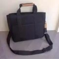 Black canvas tote bag detail, featuring durable webbed handles and brown leather grip. - Black