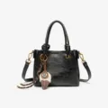 Stylish black leather handbag featuring top handles, crossbody strap and ice cream charm. - Black