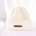 Close-up detail of warm beige knitted winter beanie hat with brown leather label accent. - M (56-58cm) / Cream