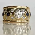 Detaillierte Nahaufnahme des breiten goldfarbenen Rings mit Zirkon und blauen Saphiren. - Größe 6 / A205 Gold