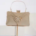 Détail de pochette de soirée dorée avec ornement de fleur en strass et pompon en métal. - Or