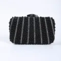 Detailed close-up shot of black beaded evening clutch with rhinestone stripes and metal clasp. - Black