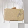 Close-up of the elegant gold glitter evening clutch featuring sparkling crystal bow and tassel. - Gold