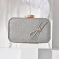 Elegant silver glitter evening clutch bag featuring a dazzling rhinestone knot detail and gold clasp. - Silver