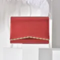 Detailed view of red evening clutch bag with elegant gold wave trim and refined texture finish. - Red