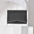 Close-up detail shot of black textured evening clutch featuring decorative metal scalloped edge. - Black