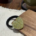 Close-up detail of a sparkling yellow rhinestone heart hair tie with black band for elegant styling. - Yellow
