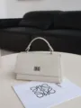 Off-white leather top-handle bag with metal turn-lock closure and elegant minimalist style. - White