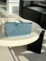 Detailed shot of light blue leather handbag showcased on modern white table in interior setting. - 24*6*17CM / Blue