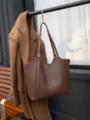Detail shot of brown leather tote bag with shoulder strap and metal buckle hanging on wall hook. - Top 40/Bottom 31*9*28CM / Coffee