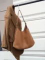 Nahaufnahme der braunen Leder-Hobo-Tasche hängend mit Mantel vor moderner architektonischer Wand. - Goldbraun