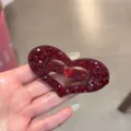 Gros plan d'une pince à cheveux cœur en strass rouge étincelant, design en cristal. - Rouge