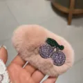 Vue détaillée d'une pince à cheveux en peluche rose avec un design de cerise en strass brillants. - Rose