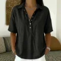 Close-up detail of black short-sleeve lapel button-down blouse worn by model in room setting. - S / Tops / Black