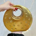 Élégante pochette de soirée ronde dorée avec strass scintillants et poignée anneau en métal chic. - Or