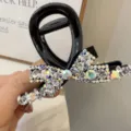 Detailed closeup of a black crystal bow hair claw clip, sparkling rhinestones glittering stylishly. - White