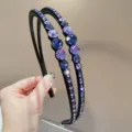 Gedetailleerd overzicht van een dubbelstrengse zwarte haarband met paarse strass-steentjes. - Paars