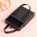 Vista detallada de la caja de joyería tipo cajón negra con asa de cinta y forro suave. - Negro (Portátil) / 9*9*3cm (Con Esponja)