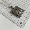 Detailed close-up shot of the silver book locket pendant necklace on a grid measuring mat. - QX-17