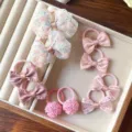 Primo piano dettagliato di simpatici elastici per capelli rosa per bambini, con fiocchi e pon-pon. - Set di 5 Paia / Rosa