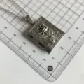 Silver vintage book locket necklace with rose relief pendant on grid background detail. - QX-9