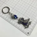 Detailed view of retro owl metal keychain with evil eye glass bead on grid measuring mat. - Owl