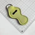 Détail de l'étui à rouge à lèvres en néoprène jaune-vert avec anneau porte-clés métallique. - Jaune