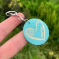 Closeup of turquoise round wooden keychain with engraved heart and mama text detail. - Style 4