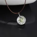 Close-up of a clear glass ball pendant necklace featuring delicate dried white flowers inside. - White Starry / Brown Chain