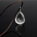 Close-up detail of a transparent teardrop glass pendant necklace featuring a real dandelion seed. - Dandelion Teardrop / Brown Chain