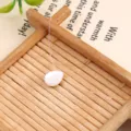 Closeup detail of the minimalist teardrop shell pearl necklace on wooden tray display. - White Mermaid Tears