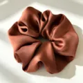 Close-up van de satijnen haarelastiek met gladde bruine stof en elegant geplooid ontwerp. - Karamel