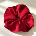 Detailweergave van levendig rode satijnen scrunchie, met gladde textuur en elegant haaraccessoire. - Rood