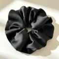 Gedetailleerde close-up van een elegante zwarte satijnen haarscrunchie met gladde textuur. - Zwart