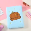 Fluffy blue notebook detail shot featuring cute embroidered capybara cover design and soft texture. - Blue