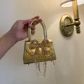 Elegante goldene Mini-Handtasche mit funkelnder Strass-Schleife und zarten Fransen. - Gold