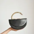 Detailed view of the black snakeskin evening bag with a unique gold snake handle design. - Black