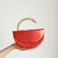 Detaillierte Nahaufnahme der roten Schlangenhaut-Clutch mit goldenem Schlangengriff. - Rot