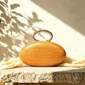 Close-up detail of luxury oval handbag with crocodile texture and gold metal ring handle. - Orange