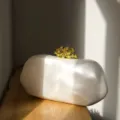 Nahaufnahme der unregelmäßigen ovalen Abendtasche mit luxuriösem goldenen Korallenverschluss. - Matt Hellgrau