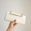 Close-up detail of the elegant white evening clutch featuring a sparkling rhinestone gold clasp. - White