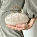 Detailansicht der französischen Marmor-Ovali-Clutch mit edlem Metallring und schicker Textur. - Milchweiß