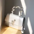 Detailansicht der silbernen metallischen Handtasche mit einzigartigem wellenförmigen Griff. - Silber