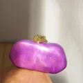 Detailansicht einer violetten marmorierten Harz-Abendtasche mit goldenem Korallen-Verschluss. - Flüssiges Lila
